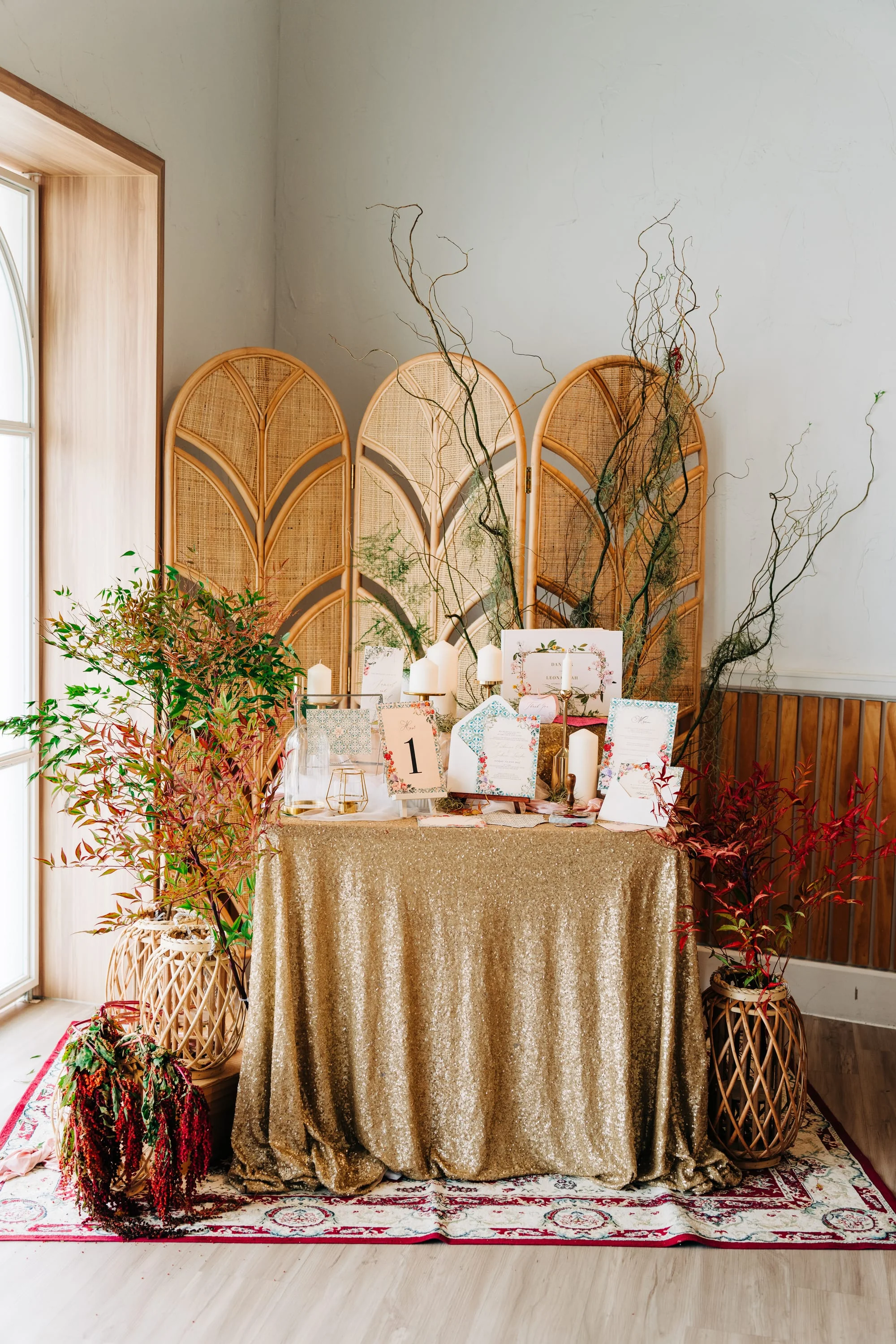 Elegant reception welcome table with gold sequin tablecloth, rattan folding screen backdrop, wedding stationery display with candles and floral arrangements
